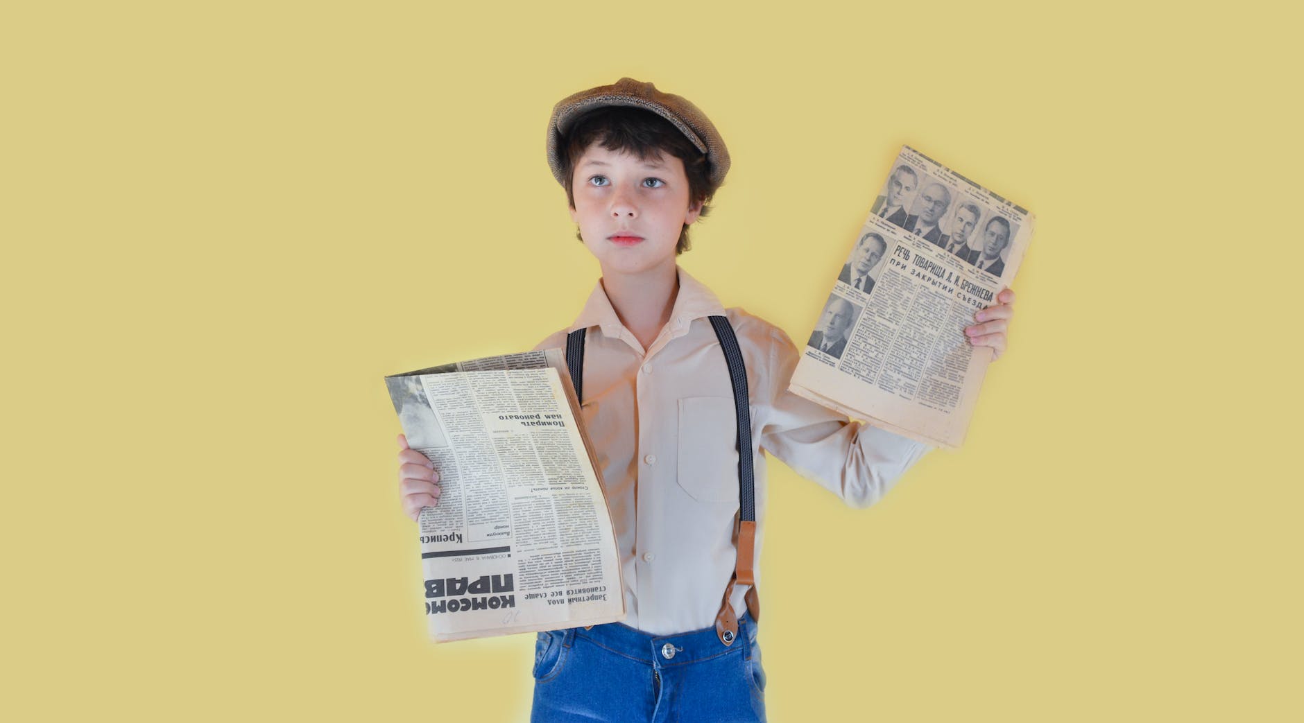 pensive boy standing with old newspapers against yellow background